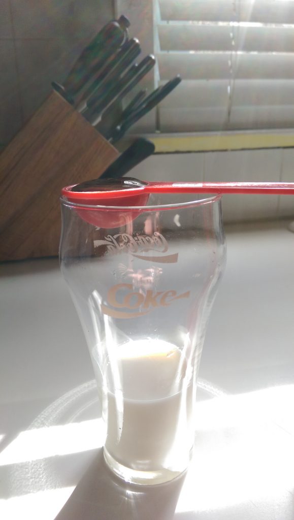 An old style Coca~Cola glass with a 1/4 Cup of 2% milk and 1 Tablespoon of syrup ready to mix
